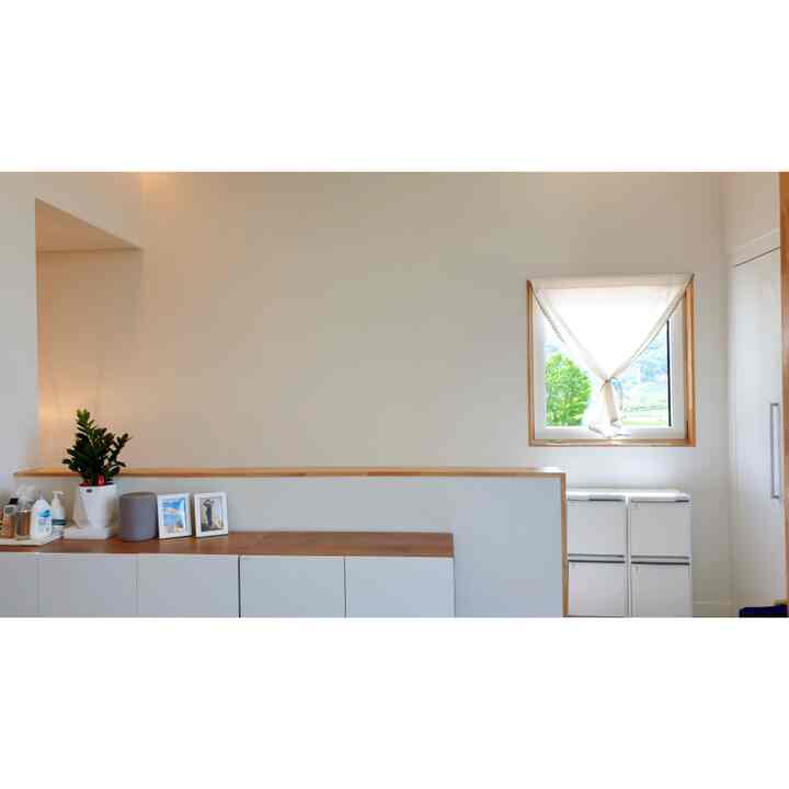 White and natural tone entrance space featuring a window with sheer curtain and neat recycling bins, creating a simple and organized interior