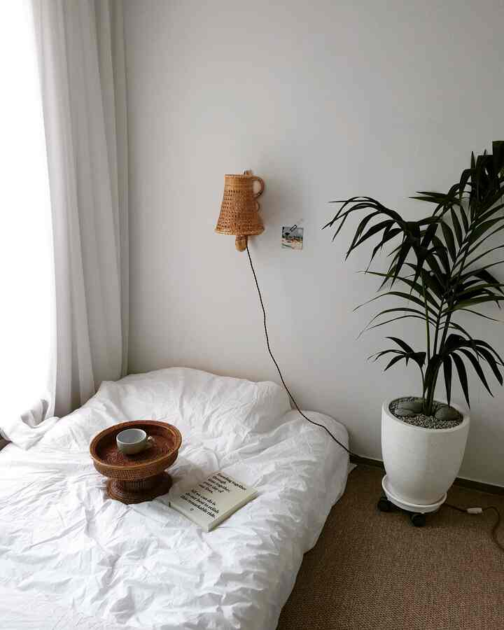 White and brown toned bedroom featuring mattress, rattan lighting, and a plant creating a simple natural atmosphere