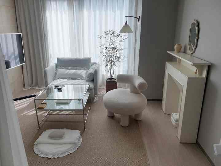 A clean and natural living room in white and beige tones featuring a single-seat sofa, unique armchair, and a glass sofa table