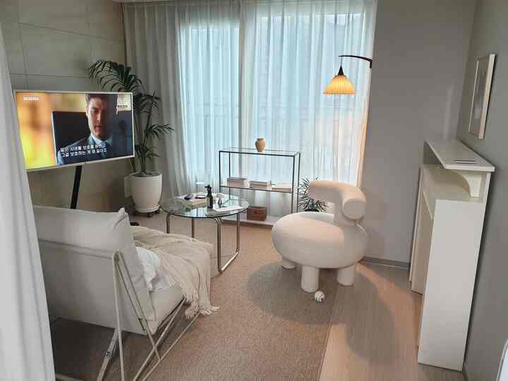 Bright white-toned living room featuring modern sofa, round glass coffee table, and comfortable armchair in a cozy, clean space