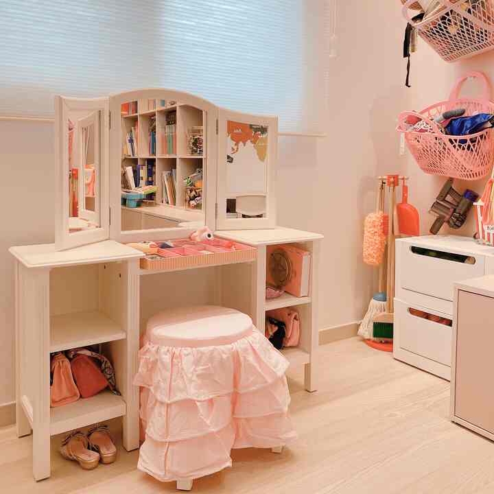 Beige-toned kids' room featuring a white vanity with triple mirrors, side storage units, and a pink ruffle-covered stool, creating a baby room ambiance
