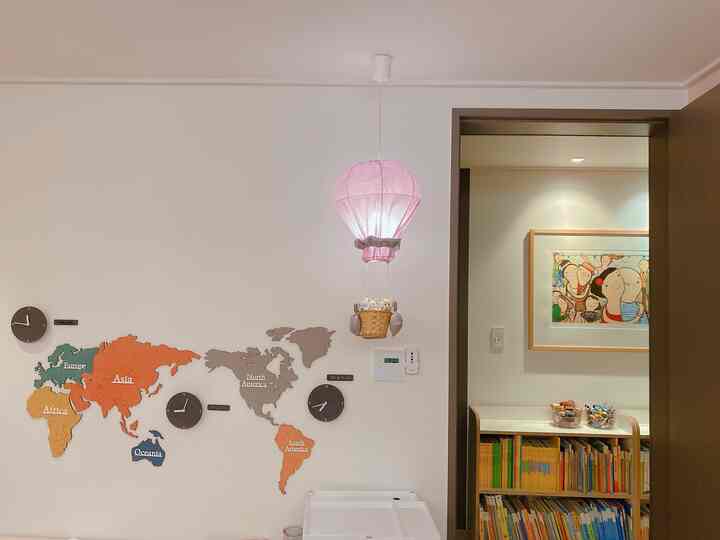 White-walled kids' room featuring a pink hot air balloon mobile, a children's bookshelf and storage unit creating a cozy and tidy atmosphere