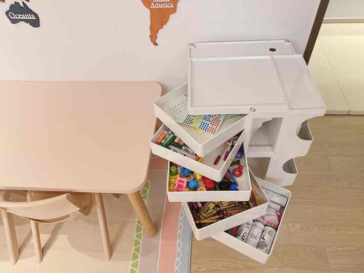 ピンクのデスクセットと木目調の床がある子供部屋、文房具を収納したホワイトトロリーが置かれた雰囲気のあるインテリア