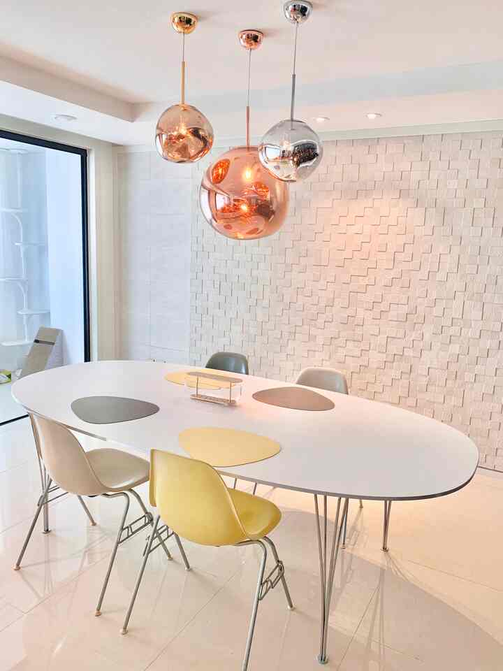 White-toned Mid-Century Modern dining room featuring a large oval dining table with Eames chairs and spherical metal pendant lights