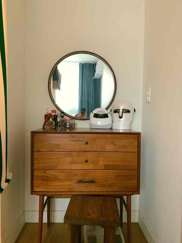 Simple and natural walk-in closet vanity featuring warm brown wood tones and a round mirror creating a cozy atmosphere