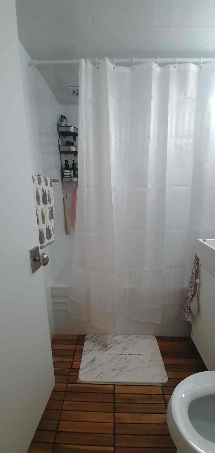 White and wood-tone bathroom featuring white shower curtain, wooden floor slats, and towel rack in a clean space