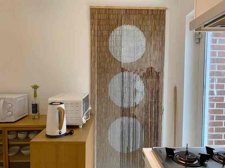 Simple kitchen space with white walls, wood tone cabinets, and a bamboo curtain featuring microwave and electric kettle