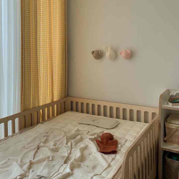 ベージュとアイボリーのトーンの子供部屋、ナチュラルな木製の幼児用ベッドにクールマットレスとリネンブランケットが配置された雰囲気のあるインテリア