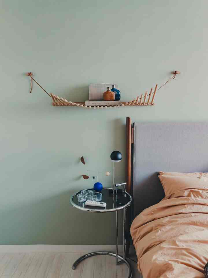 A simple bedroom with soft green walls and a light gray bed, featuring a chrome side table and minimalist decor creating a harmonious space