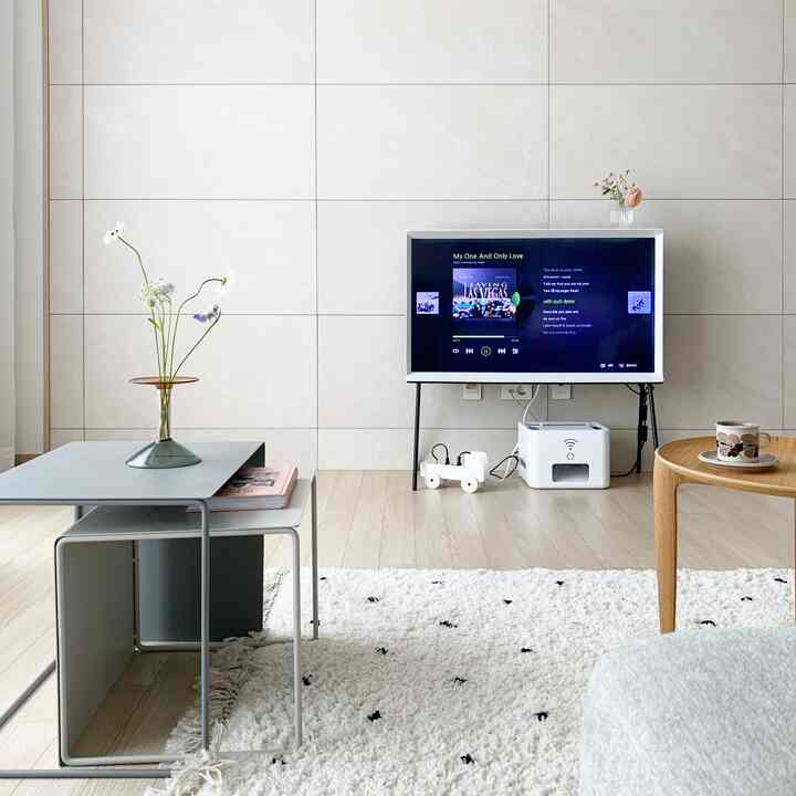 A white and natural toned living room featuring minimal tray tables and TV stand in a clean, serene space