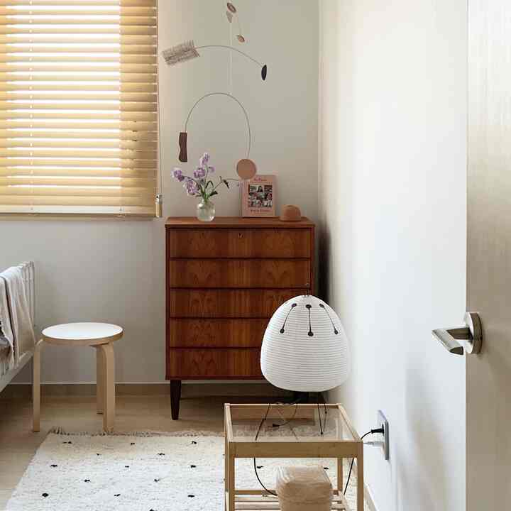 Natural-toned kids' room featuring a wood nightstand, stool, mobile, and table lamp creating a cozy atmosphere