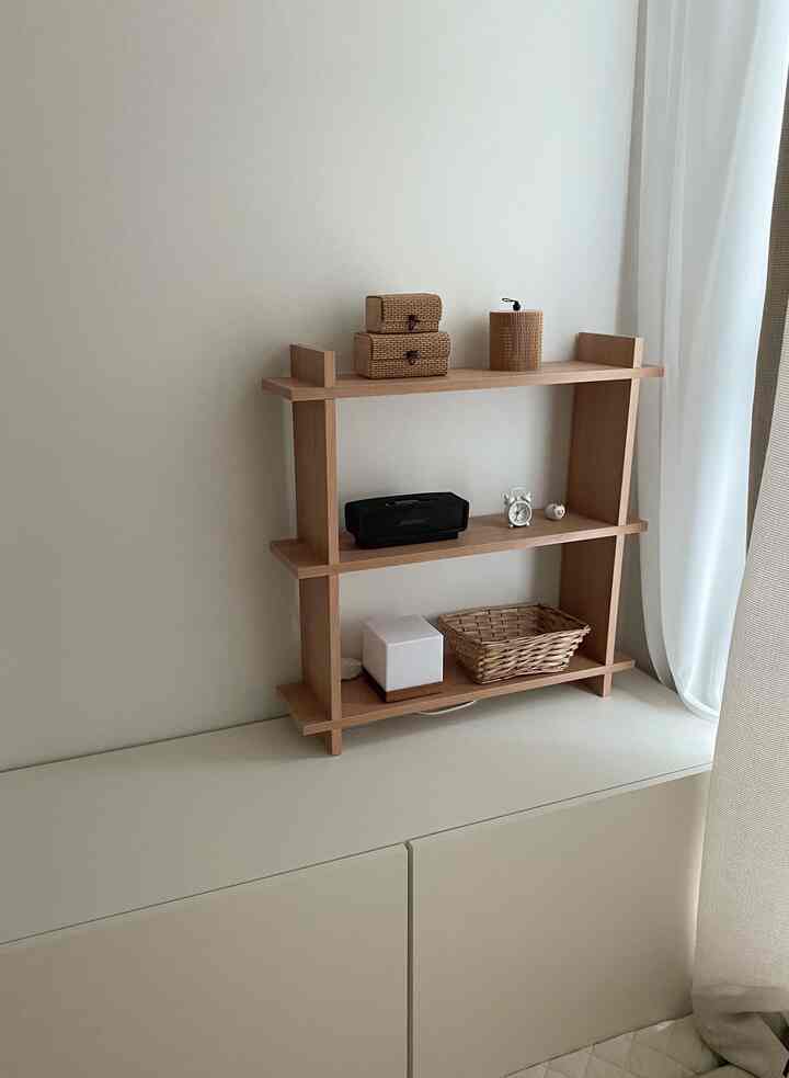 Natural wood tone shelf with white bedroom walls and curtains, storage space for baby items in a bedroom shared with a baby