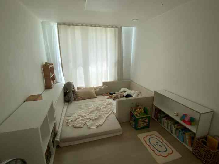 白とナチュラルカラー調の縦長の子供部屋、ベッドと遊び場が配置された赤ちゃんに優しい空間