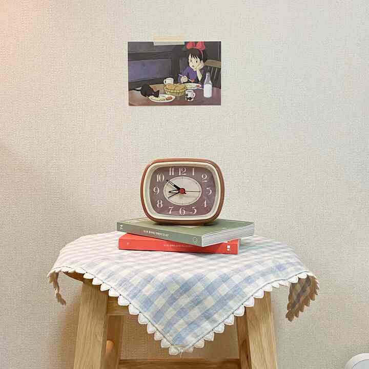 明るくナチュラルなトーンの寝室空間、木製DIYスツールの上にチェック柄のキッチンクロスとヴィンテージの置き時計が置かれた落ち着いたインテリア