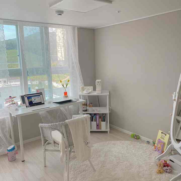 White-toned small loft officetel room featuring a desk and armchair by window, built-in closet and rug creating a cozy home cafe space