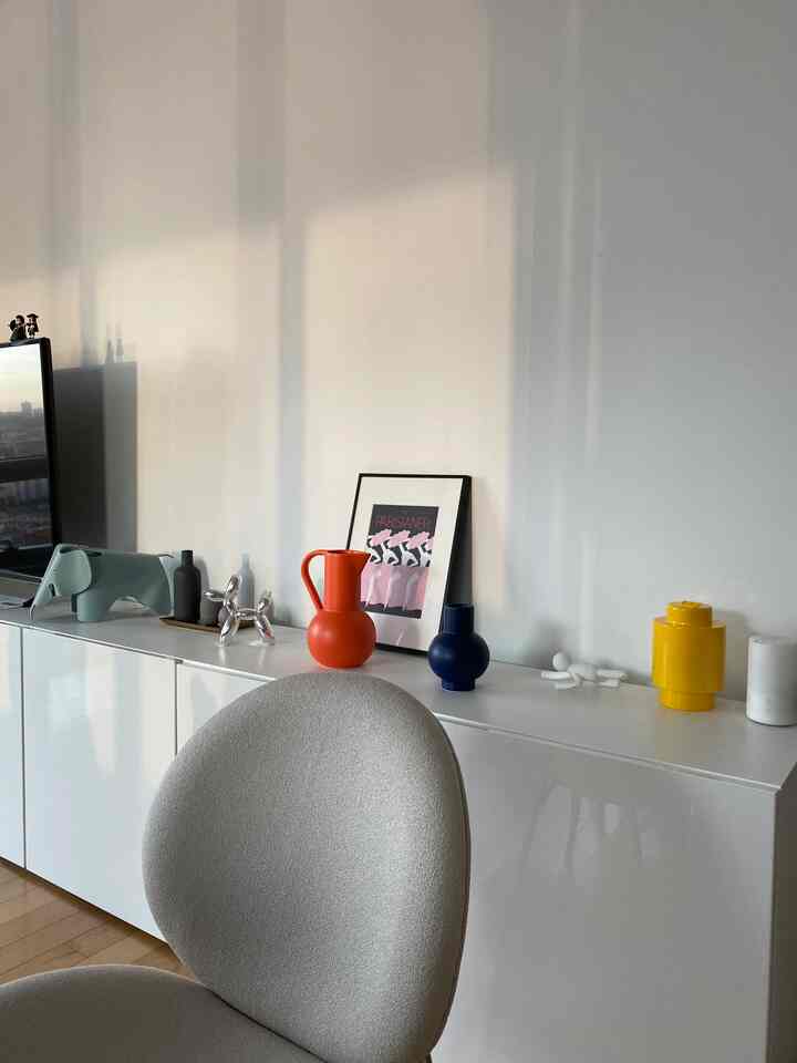 白を基調としたモダンなリビング、カラフルなオブジェが並ぶ白いキャビネットの印象的な空間