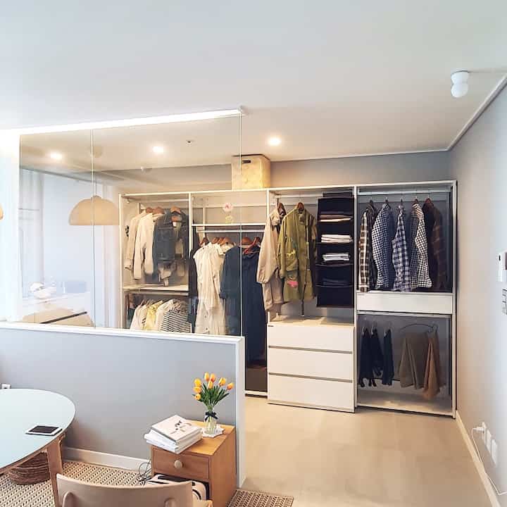 Bright and clean walk-in closet space in white and beige tones featuring built-in closets and a wood-tone side table with tulip vase