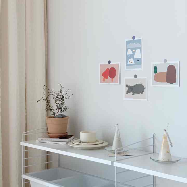 White and ivory-toned bedroom featuring fabric posters on wall and system shelf with plants and candles creating a neat space