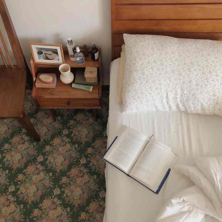 A natural-toned bedroom space featuring a wooden nightstand and floral pillow with cozy atmosphere