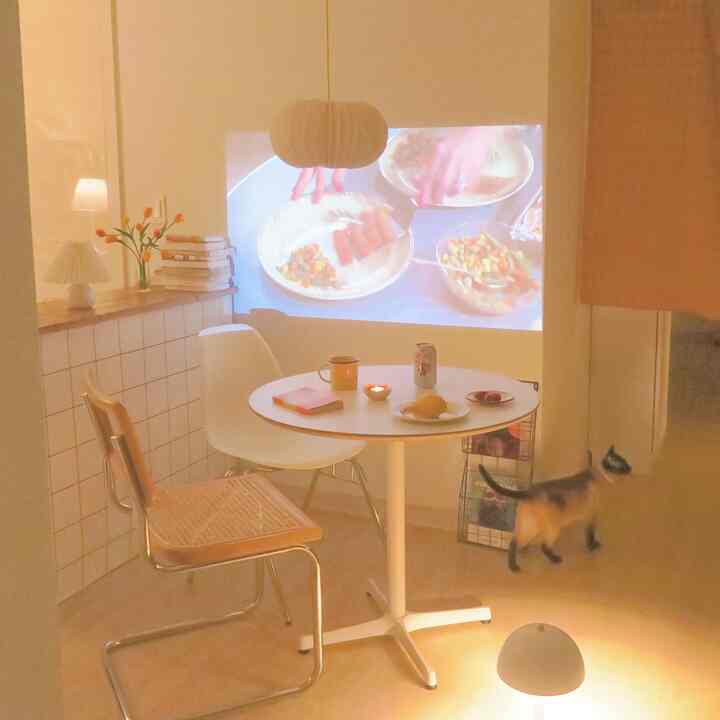 Natural-toned kitchen featuring a round dining table, different chairs, and a projector casting images on the wall with warm lighting