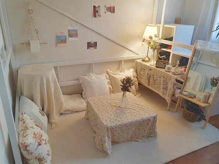 Cozy bedroom in ivory and natural tones featuring a floor lamp, table with floral cloth, and cushions with a warm, natural atmosphere