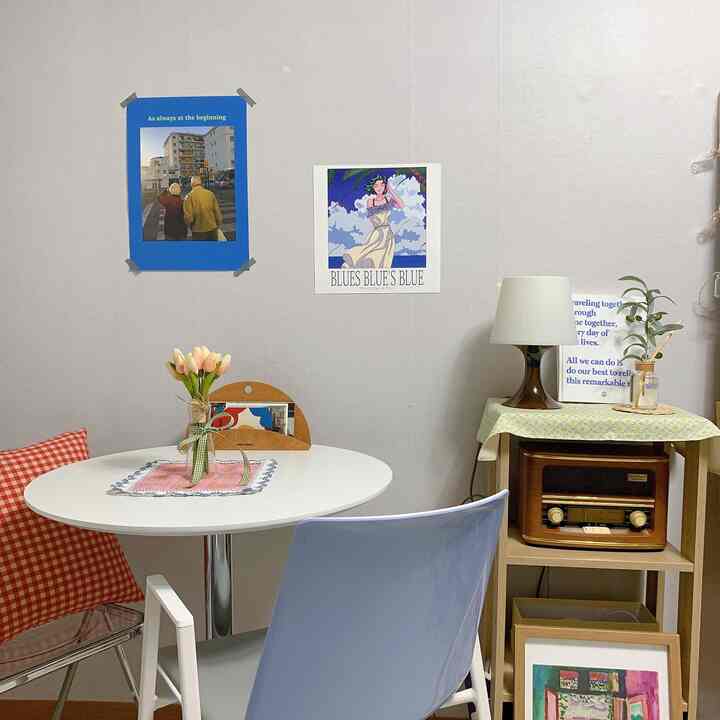 明るいグレーの壁と白い円形テーブル、透明と青の椅子、レトロなスピーカーを配した居心地の良いワンルームのインテリア