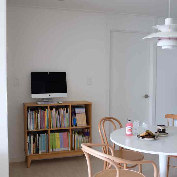 白を基調としたリビング兼ダイニング、木目調の本棚と丸いダイニングテーブルが配置されたナチュラルでシンプルなインテリア