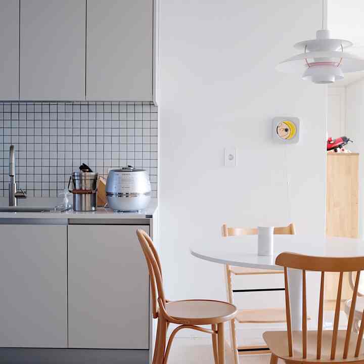 Minimal dining space featuring a white linear kitchen and round table with wooden chairs, blending white and wood tones