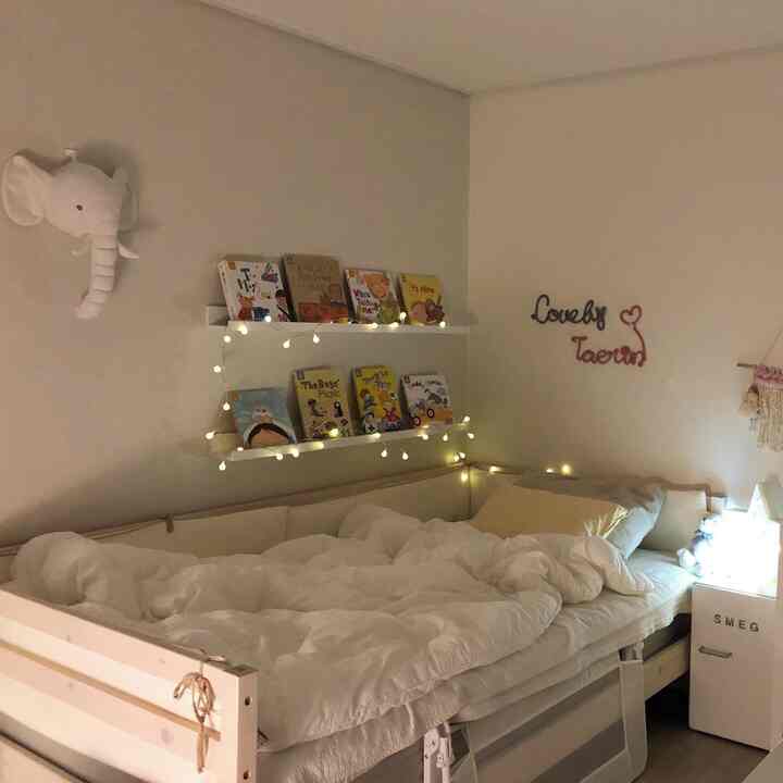 白とベージュの色調の子供部屋、木製のデイベッドと壁棚に子供向けの本とLEDライトが温かみのある雰囲気を演出する空間