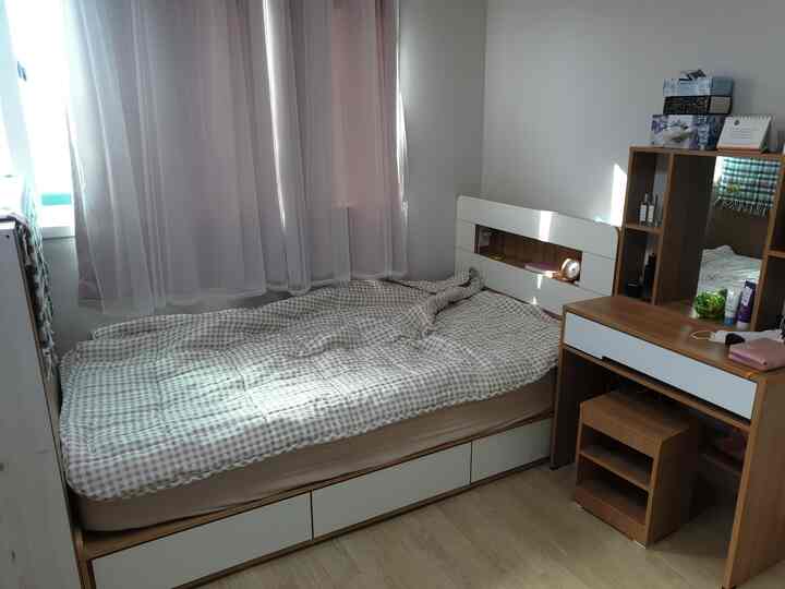 Cozy bedroom with white walls and wood tone furniture, featuring beige checkered duvet and pink curtains
