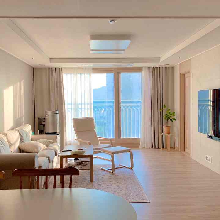 ホワイトと木目調のリビング、ソファ、アームチェア、カーテン、植物が配置された温かみのある雰囲気のインテリア