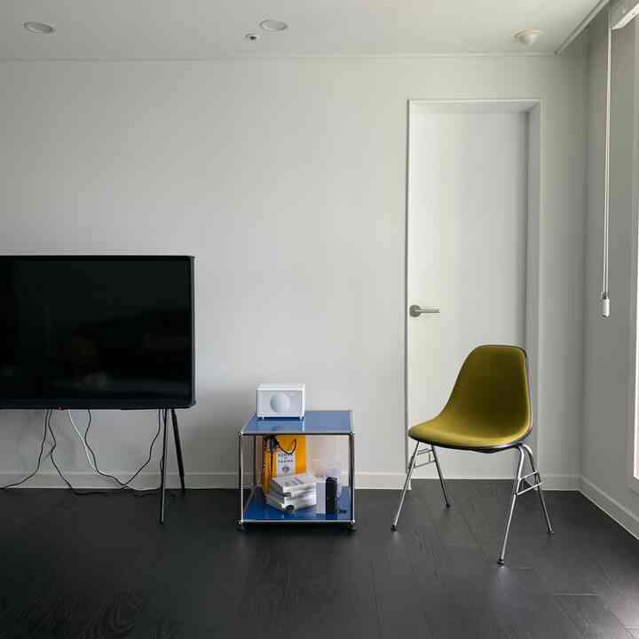 Living room with white walls and dark brown floor, featuring a blue side table and vintage-style chair in a simple setting