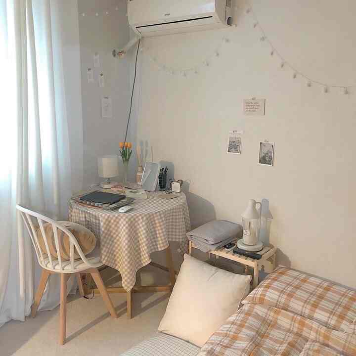 A small studio room in soft beige and ivory tones, featuring a checkered table and bedspread, neat home office and home cafe setup