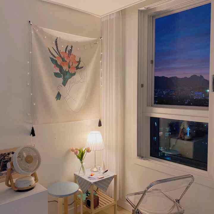 アイボリーと木目調が調和した小さな空間、窓際に透明な椅子とサイドテーブルの照明が配置された落ち着いた読書コーナー