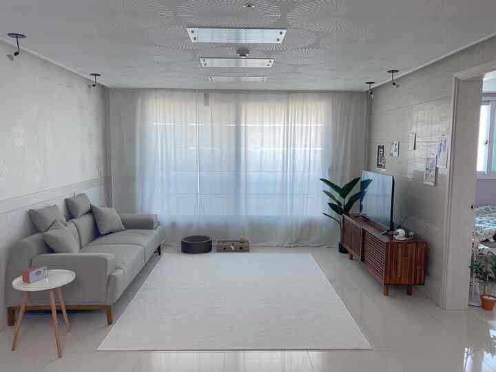 Bright living room in white and natural modern tones featuring a gray sofa and wood tone TV stand, clean and minimalistic atmosphere
