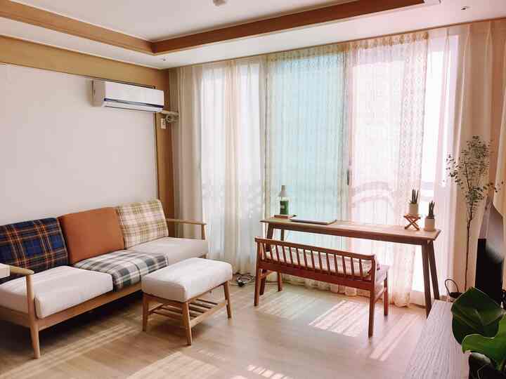 木目調とホワイトのリビングルーム、カラフルなクッションが置かれた木製ソファと整ったカーテンが配置された自然な雰囲気のインテリア