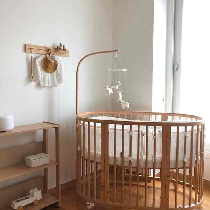 Natural and wood tone newborn baby room featuring a round wooden crib and wooden shelves, creating a cozy atmosphere