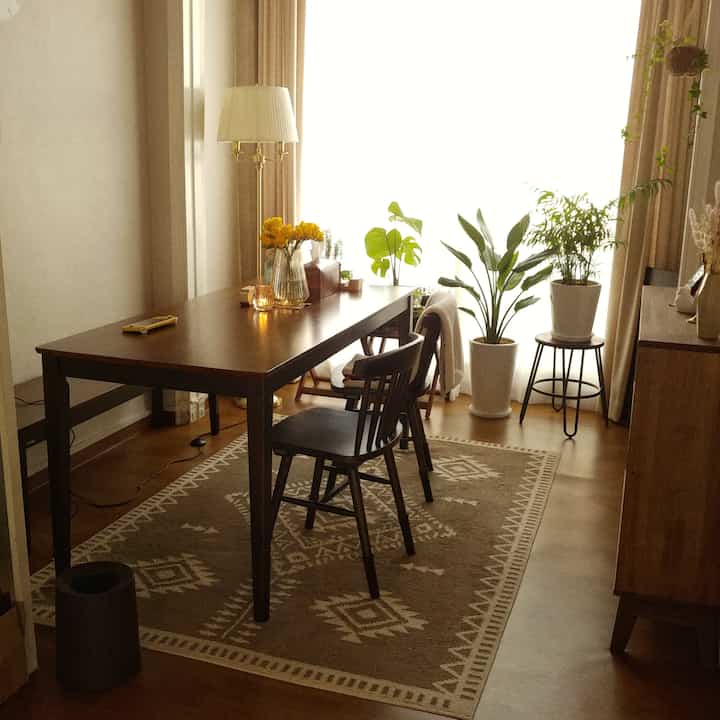 Natural wood tones and beige dining room featuring a wooden table, chairs, and lush green plants creating a cozy atmosphere