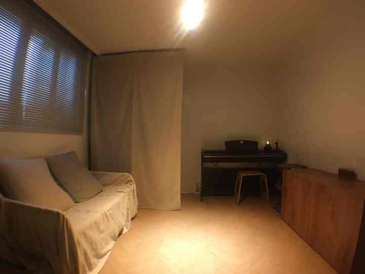 Beige and wood tone small living room featuring sofa, fabric partition, and digital piano with simple interior