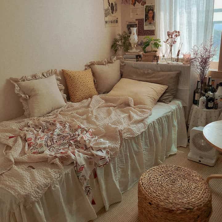 Beige-toned small bedroom featuring a rattan stool, cushions, and bedskirt creating a cozy atmosphere