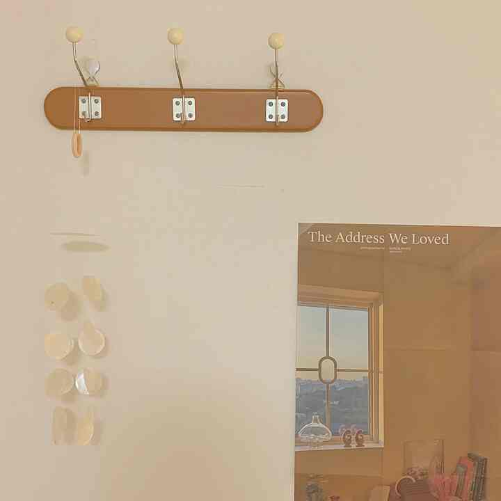 Beige-toned wall featuring a wood-toned coat rack, shell mobile, and a poster showing window scenery in a cozy space