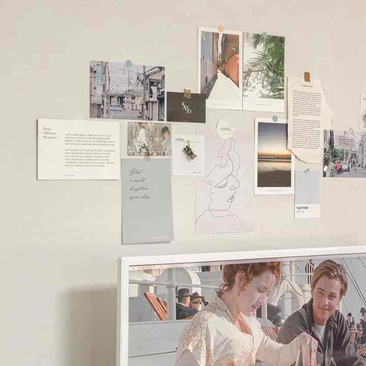 Soft white-toned wall featuring assorted emotional postcards and posters in a cozy home office space