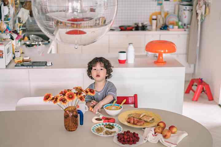 White and red toned kitchen with a child seated at the dining table, showcasing a modern natural atmosphere