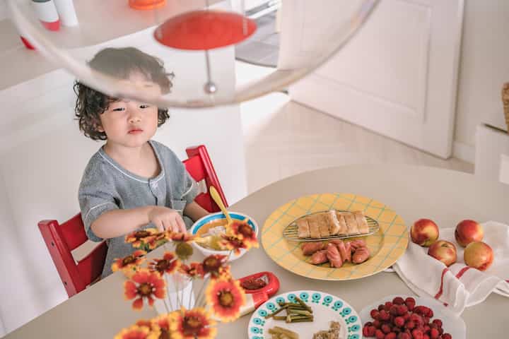 Soft white-toned dining room featuring a child seated on a red chair eating at the dining table, creating a warm atmosphere