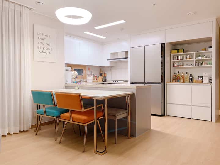Bright white and silver kitchen in a newlywed home, featuring colorful chairs and organized storage cabinets