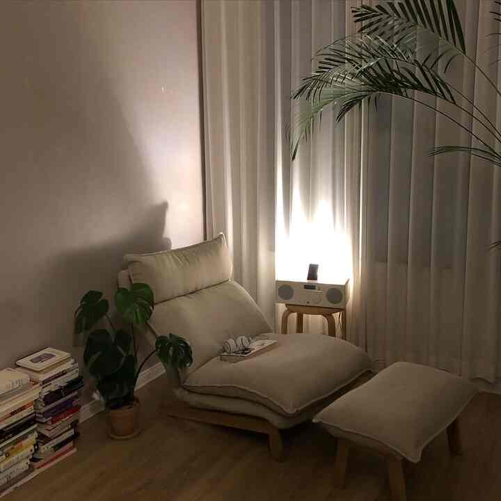 Beige high-back recliner sofa with ottoman, wood tone flooring and plants in a natural modern living room space