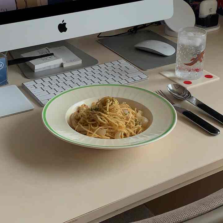 ナチュラルなベージュ色調のホームオフィスデスクに、パスタの皿とコップが置かれた一人暮らし向けの空間