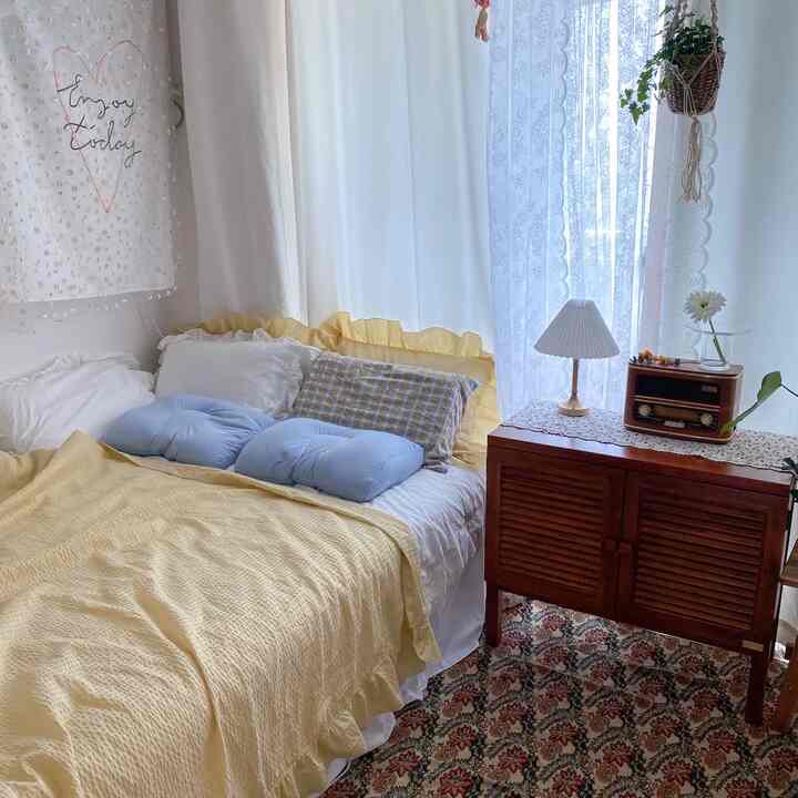 Bright and airy white and yellow toned bedroom featuring bed with yellow duvet and pillows, retro wooden cabinet, creating a cozy atmosphere