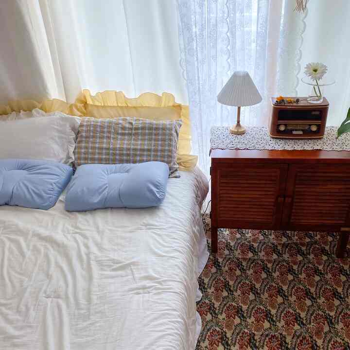 White and yellow toned bedroom featuring a bed with pillows and bedding alongside a retro console table, creating a cozy atmosphere