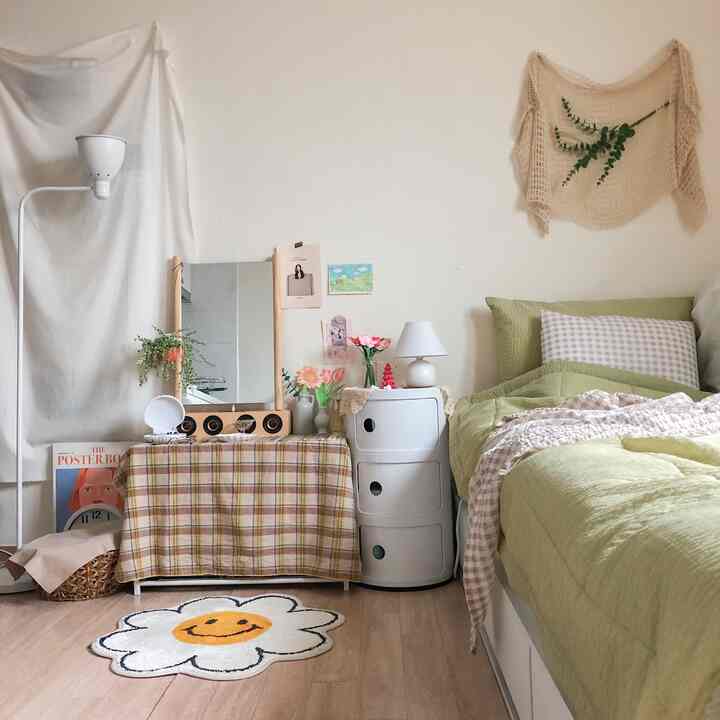 Beige and wood-tone studio bedroom featuring green bedding, round storage unit, and flower-shaped rug creating a cozy atmosphere